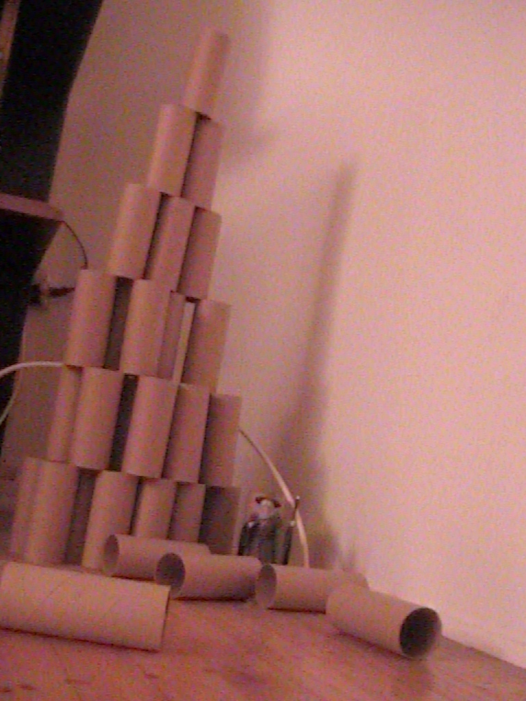 A tower of toilet paper rolls with a gandaulf figureine standing at the bottom